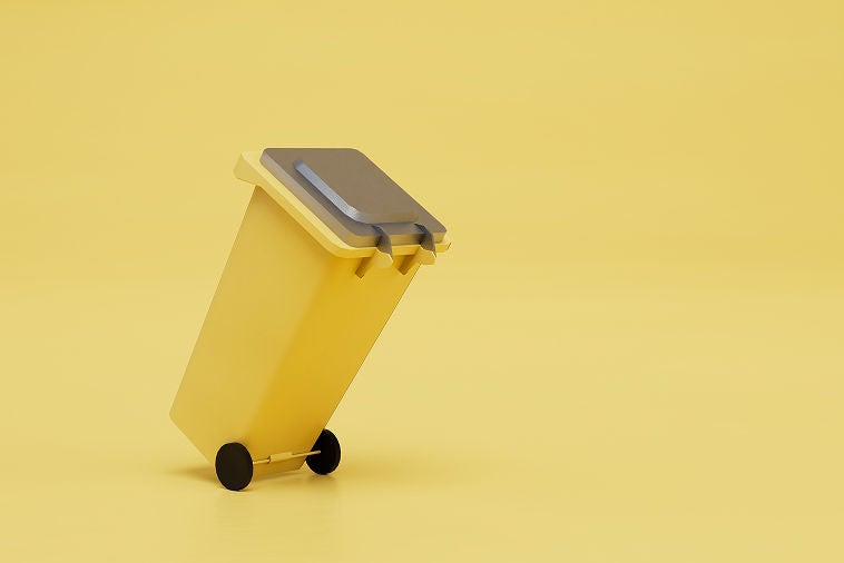Contenedor de basura amarillo con ruedas inclinada sobre un fondo amarillo