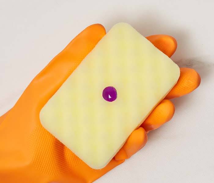 Esponja amarilla con gota de detergente morado y guante de limpieza.